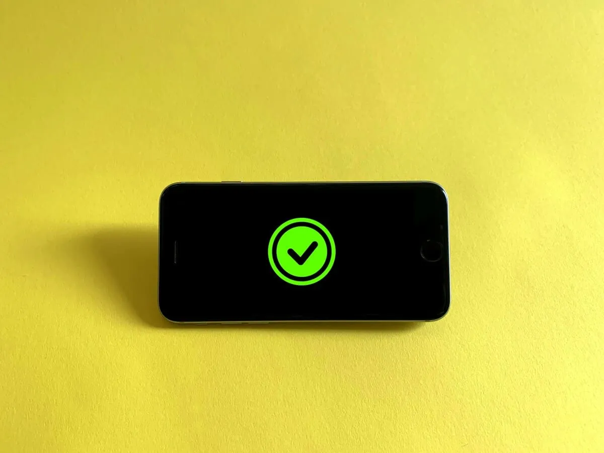 Black phone with green checkmark on screen, placed on yellow background