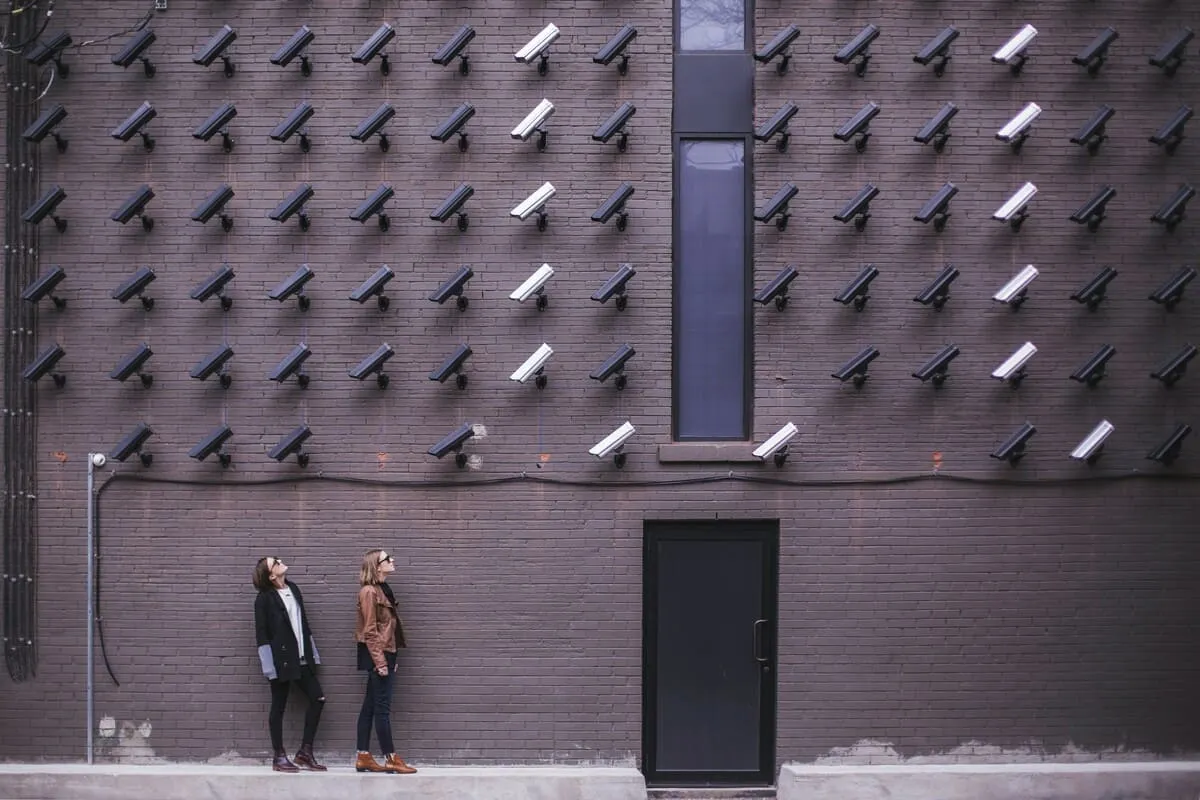 Two women facing security camera above mounted on building